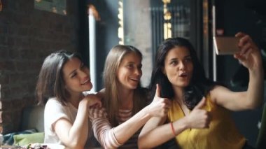 Mutlu genç bayanlar kafede gülerek başparmak-up jest ile selfie çekmek