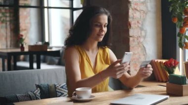 Heyecanlı kız tek başına kafede oturan akıllı telefon ve kredi kartı ile online ödeme