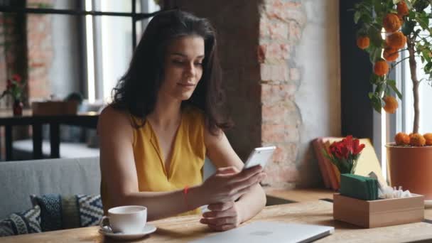 Charmig ung dam håller smartphone röra skärmen leende i moderna café — Stockvideo