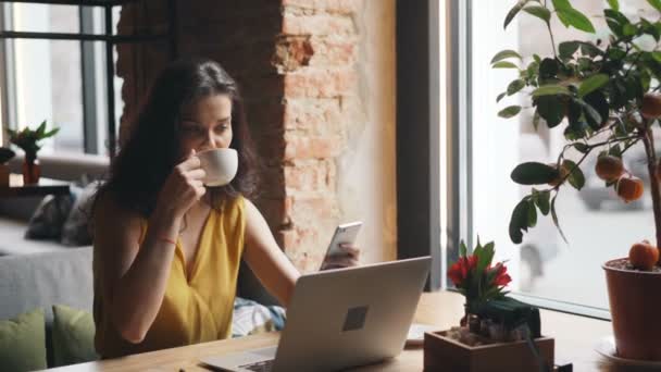 Roztomilá mladá žena konzumace čaje pomocí telefonu Smartphone v kavárně relaxační úsměv — Stock video