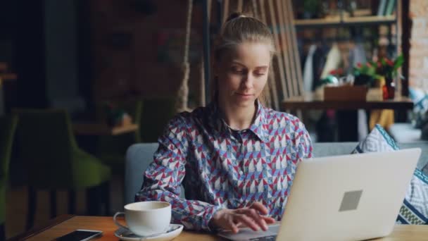 Joyeux jeune femme qui travaille avec un ordinateur portable dans un café tapant assis à table seule — Video