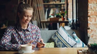 Kafede akıllı telefon ekranına dokunan neşeli kız sesli mesaj göndererek konuşuyor