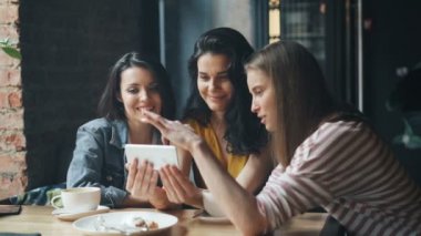 Kafede eğlenirken gülümseyerek akıllı telefon ekranına bakan neşeli kızlar