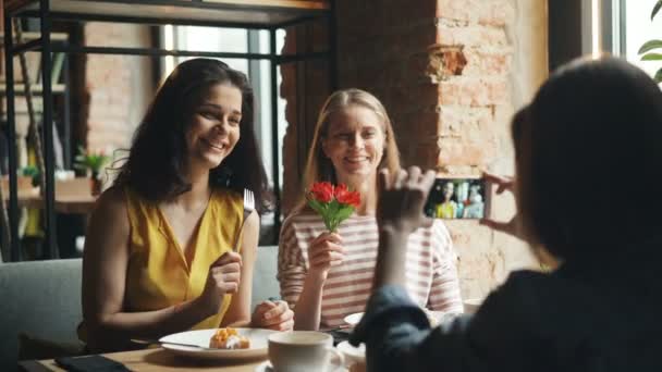 Beztroskich kobiet stwarzających dla kamery smartphone w kawiarni gospodarstwa kwiat zabawy — Wideo stockowe