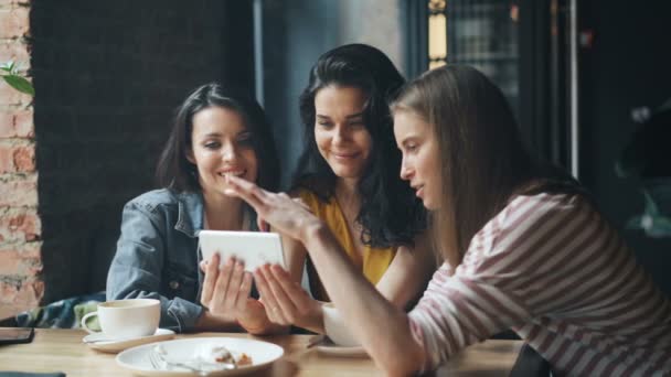 Радісні дівчата, дивлячись на екран смартфона, посміхаючись, розважаються в кафе — стокове відео