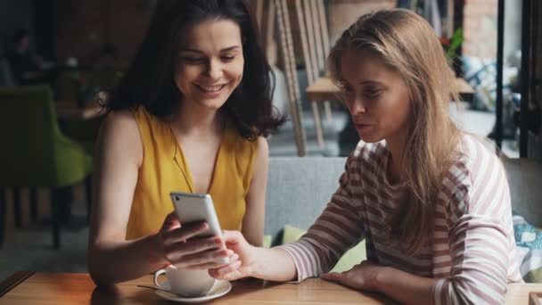 Joyful friends looking at smartphone screen in cafe talking laughing having fun — Stock Video