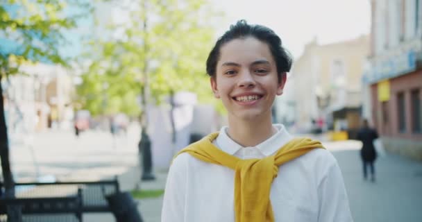 Портрет красивого мальчика, улыбающегося, смотрящего в камеру, стоящую на улице в одиночестве — стоковое видео