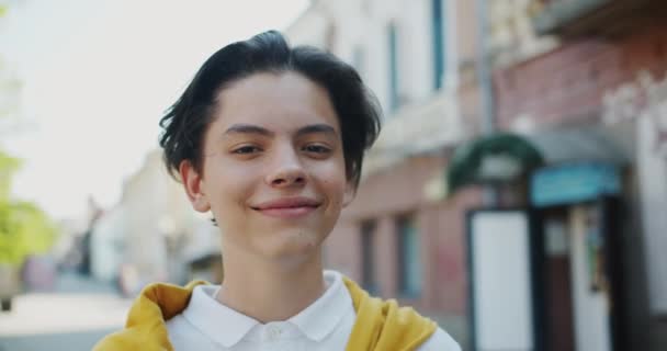 Крупный план портрета радостного подростка, улыбающегося на улице, смотрящего в камеру — стоковое видео