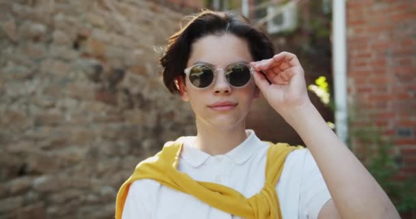 Slow Motion portret van Teenage Kid opstijgen zonnebril glimlachend buitenshuis — Stockvideo