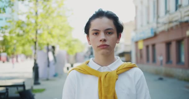 Портрет привлекательного подростка, стоящего на улице с серьезным лицом, а затем улыбающегося — стоковое видео