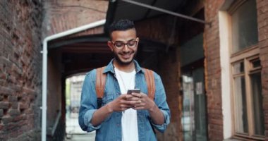 Arap öğrencinin akıllı telefon kullanarak yavaş hareket ve açık havada ayakta gülüyor