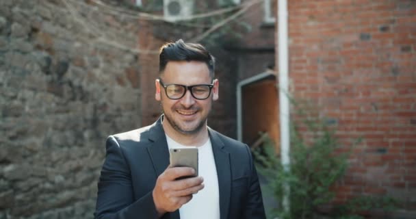 Chico barbudo guapo usando mensajes de texto de teléfonos inteligentes al aire libre en la calle — Vídeos de Stock