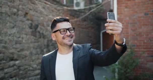 Neşeli orta yaşlı adam açık havada gülümseyerek akıllı telefon kamerası ile selfie çekerek — Stok video