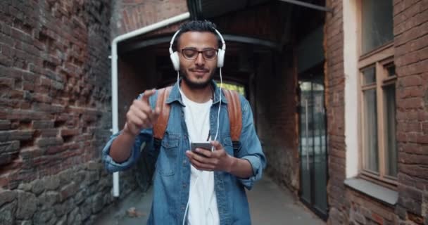 Cámara lenta de hipster árabe disfrutando de la música en auriculares bailando al aire libre — Vídeo de stock