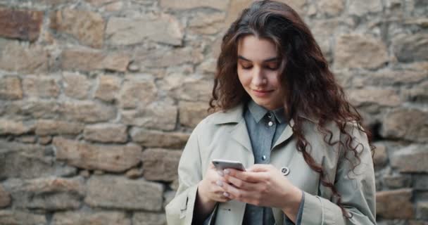 Cámara lenta de chica bonita usando teléfono inteligente en la calle tocando la pantalla sonriendo — Vídeo de stock