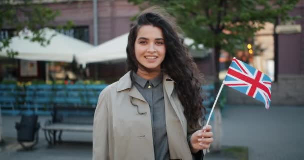 Porträtt av lycklig flicka stående utomhus med brittisk flagga leende på blåsig dag — Stockvideo