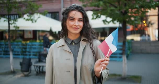 Portrait d'une étudiante attirante debout à l'extérieur avec le drapeau national français — Video