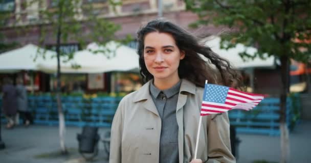 Медленный портрет красивой девушки с американским флагом, улыбающейся на улице — стоковое видео