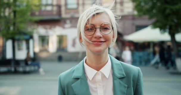 Медленный портрет веселой блондинки, стоящей на улице и улыбающейся — стоковое видео