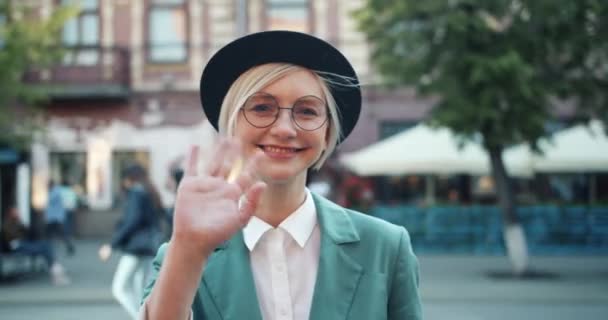 Медленное движение счастливой девушки, машущей рукой на улице, смотрящей в камеру в городе — стоковое видео