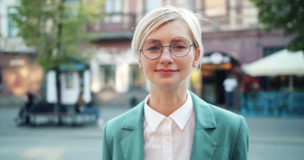 Retrato de linda mujer de negocios en gafas de pie solo en la calle sonriendo — Vídeo de stock