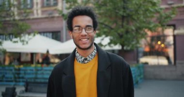 Mutlu Afro-Amerikan öğrencinin yavaş çekim portresi açık havada ayakta gülümseyen