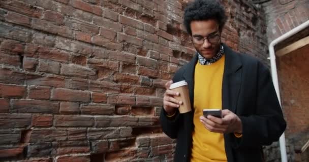 Slow Motion van African American Guy het gebruik van smartphone met koffie buitenshuis — Stockvideo