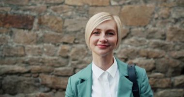 Tuğla duvar ayanında duran kameraya bakarak gülümseyen güzel sarışın Portresi