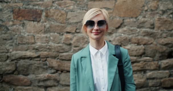 Portret van mooie stijlvolle meisje in zonnebril staande buitenshuis glimlachend — Stockvideo