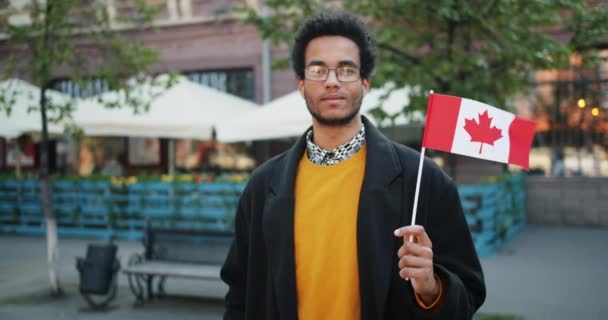 カナダの旗を持つ屋外のひげを生やしたアフリカ系アメリカ人男性のスローモーションの肖像画 — ストック動画