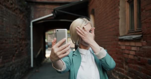 Cámara lenta de la bonita rubia tomando selfie con la cámara del teléfono inteligente al aire libre — Vídeo de stock