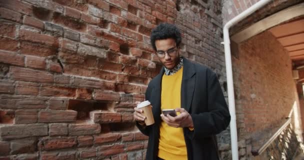 Movimento lento do estudante afro-americano bebendo café usando smartphone ao ar livre — Vídeo de Stock