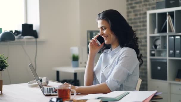 Chica alegre empleado hablando en el teléfono móvil riendo con el ordenador portátil en la oficina — Vídeos de Stock