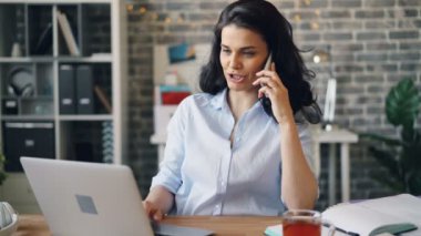 Neşeli genç esmer cep telefonu sohbet ve ofiste dizüstü bilgisayar kullanarak