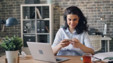 Heyecanlı genç kadın iş yerinde ekran dokunmadan akıllı telefon oyunu oynuyor