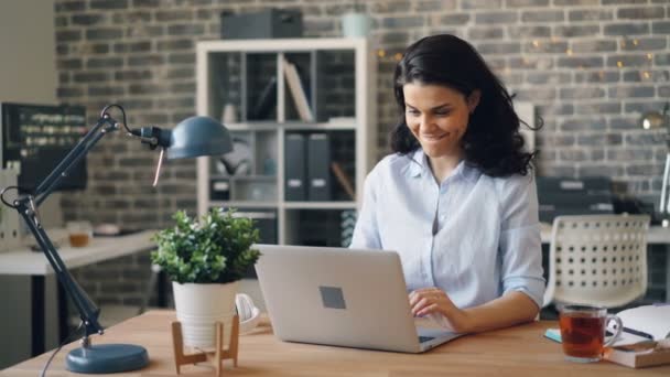 Menina feliz digitando com laptop, em seguida, relaxante alongamento braços sorrindo no escritório — Vídeo de Stock