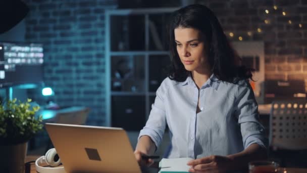 Mooi meisje werken met laptop 's nachts in Office glimlachend schrijven in notebook — Stockvideo