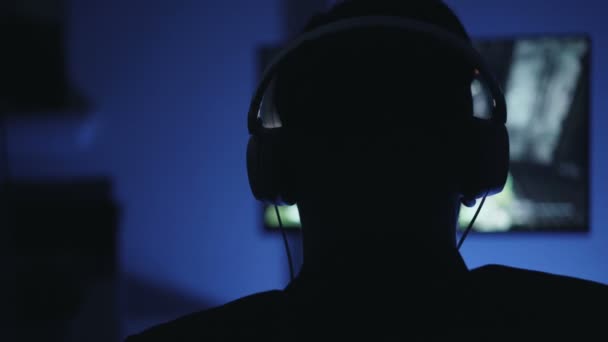 Крупним планом силует чоловічого голови в навушниках, граючи в відеогру вдома — стокове відео