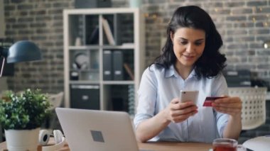 Genç kadın işyerinde akıllı telefon kullanarak kredi kartı ile online ödeme