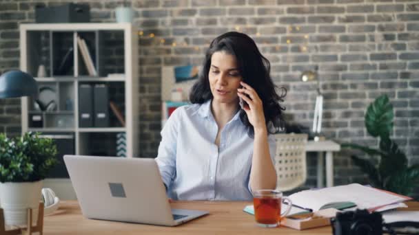 Glimlachend meisje praten op mobiele telefoon en werken met computer in moderne kantoor — Stockvideo