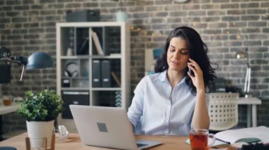 Güzel iş kadını cep telefonu konuşuyor ve ofiste dizüstü bilgisayarda yazma
