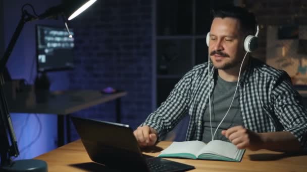 Joyful man njuter av musik i hörlurar upptagen med laptop Dans på Dark Office — Stockvideo