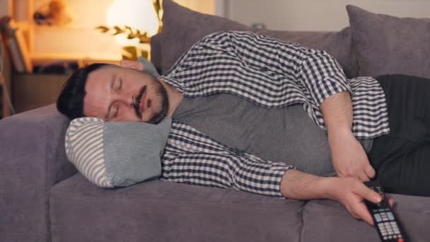 Retrato de chico en chothes casuales durmiendo en sofá en casa sosteniendo TV a distancia — Vídeo de stock
