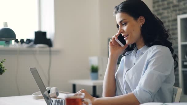 Trabajador de oficina feliz riendo hablando por teléfono móvil y trabajando con el ordenador portátil — Vídeos de Stock