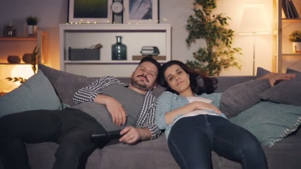 疲れて眠い人の男女がソファのあくびで家でテレビを見ている — ストック動画