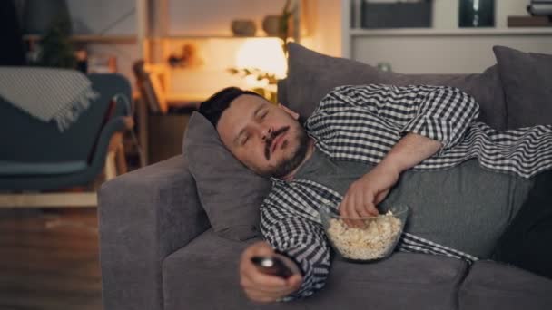 Портрет привлекательного мужчины, смотрящего фильм по телевизору ночью в уютной квартире — стоковое видео