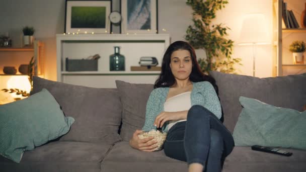 Девушка смотрит телевизор ест попкорн дома, когда мужчина прыгает из-за дивана — стоковое видео