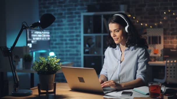 Glad arbetstagare lyssnar på musik dansa arbeta med laptop i mörkt rum — Stockvideo