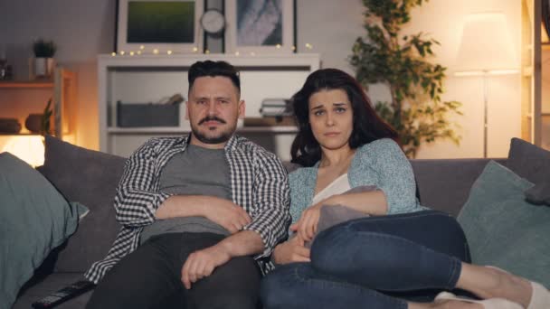 Casal de pessoas assistindo filme triste na TV sentado no sofá em casa juntos — Vídeo de Stock