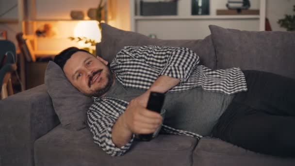 Retrato de homem alegre assistindo TV sorrindo e comendo pipocas à noite em casa — Vídeo de Stock